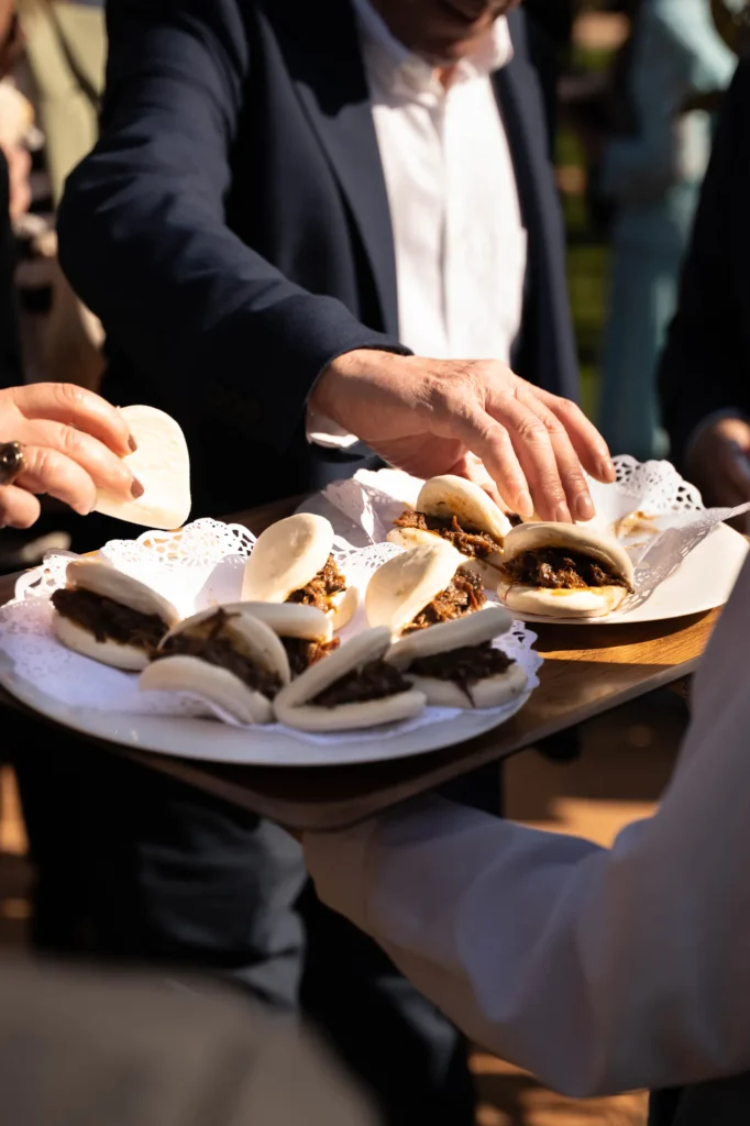 Invitados cogiendo pan bao relleno de una bandeja durante el cóctel