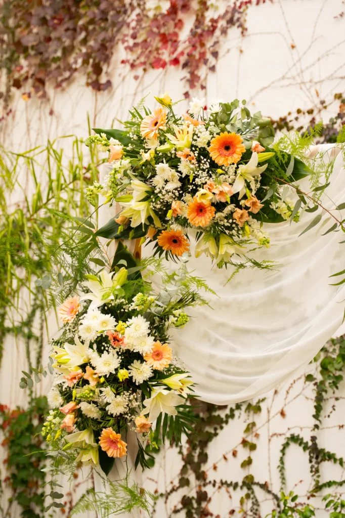 Composición de flores naranjas y blancas con telas en la decoración de una boda