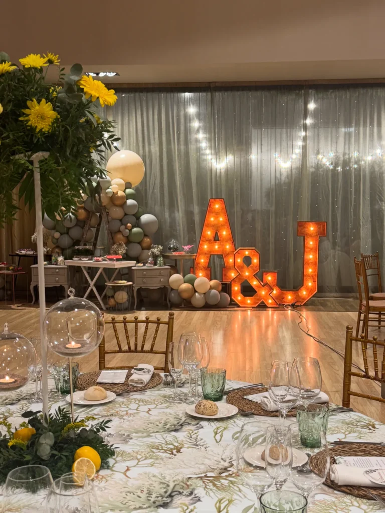 Iniciales luminosas de los novios y mesas decoradas con flores amarillas en el salón