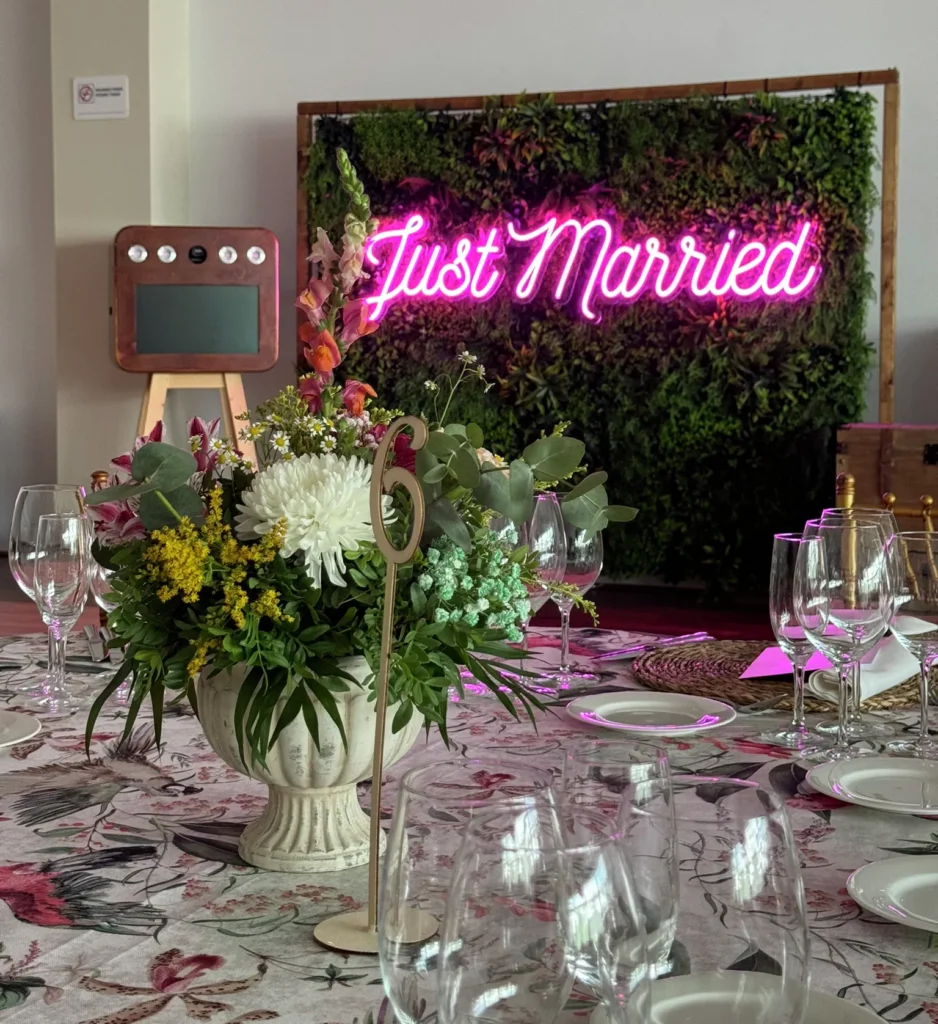 Neón Just Married sobre pared vegetal junto a una mesa decorada con flores