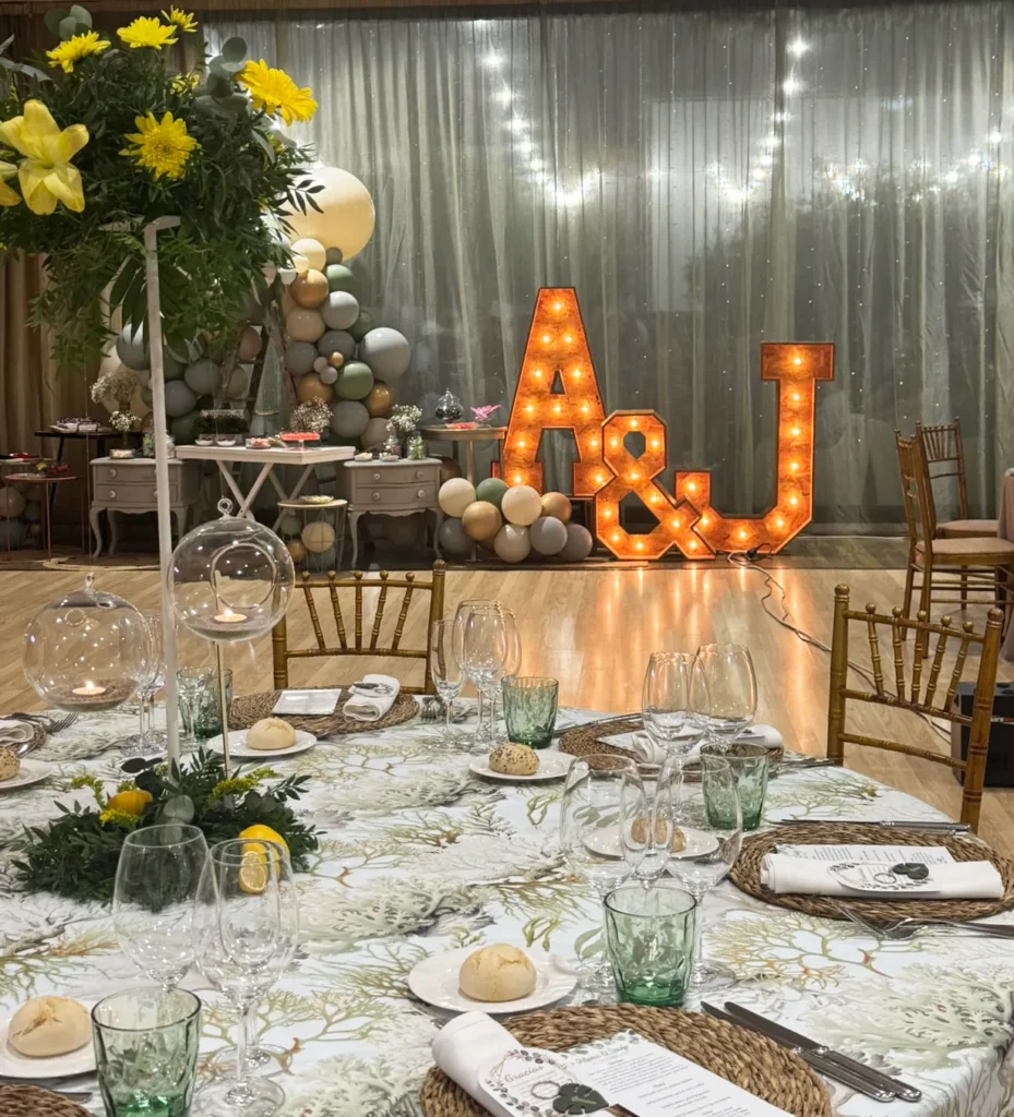 Salón de banquetes con mesas decoradas e iniciales luminosas de los novios al fondo