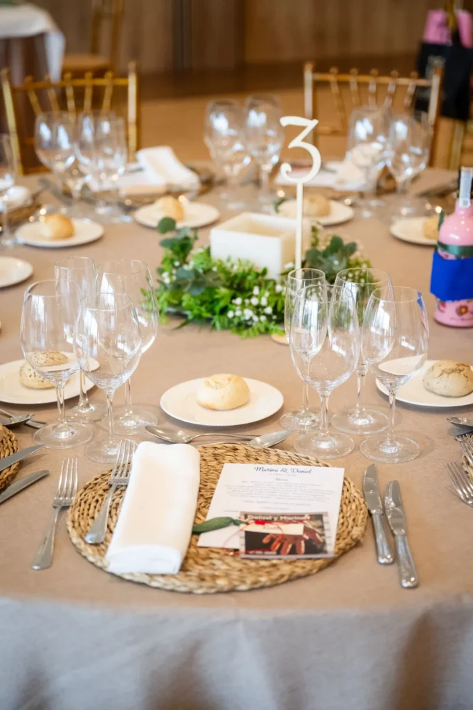 Mesa de banquete de boda con bajoplatos de fibra natural y número de mesa