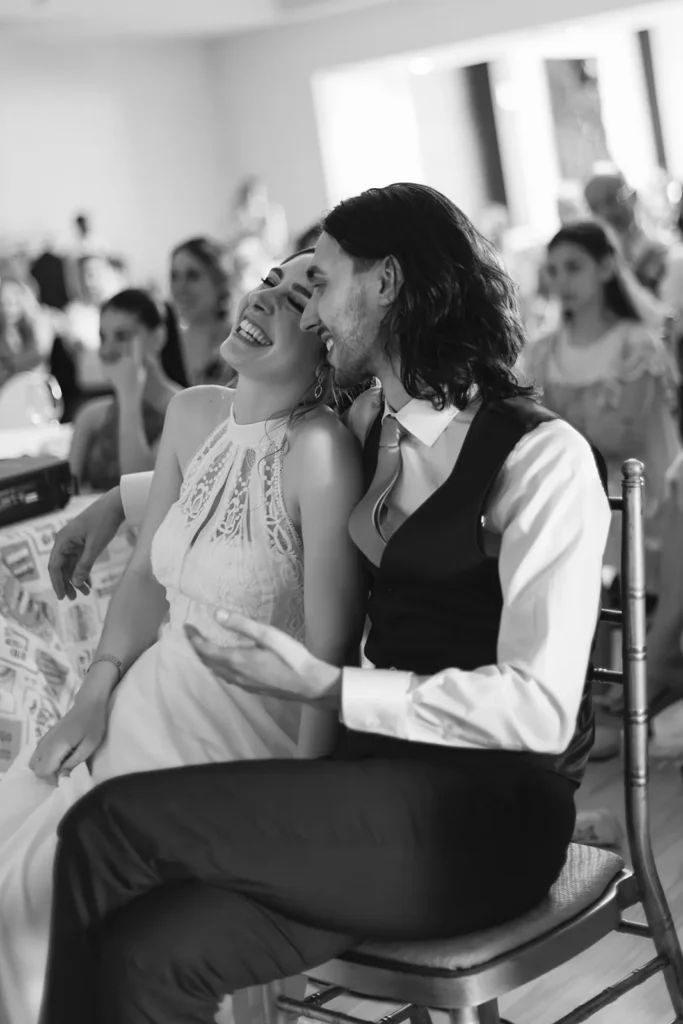 Novios abrazados y riendo durante la celebración, rodeados de invitados