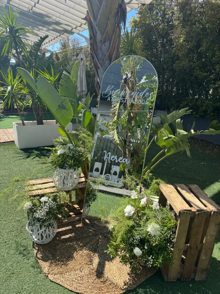 Photocall de bienvenida con plantas tropicales y cajas de madera en el jardín