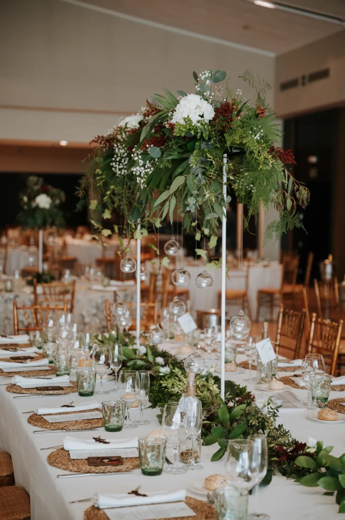 Centro de mesa alto con flores blancas y verde sobre una mesa imperial de boda